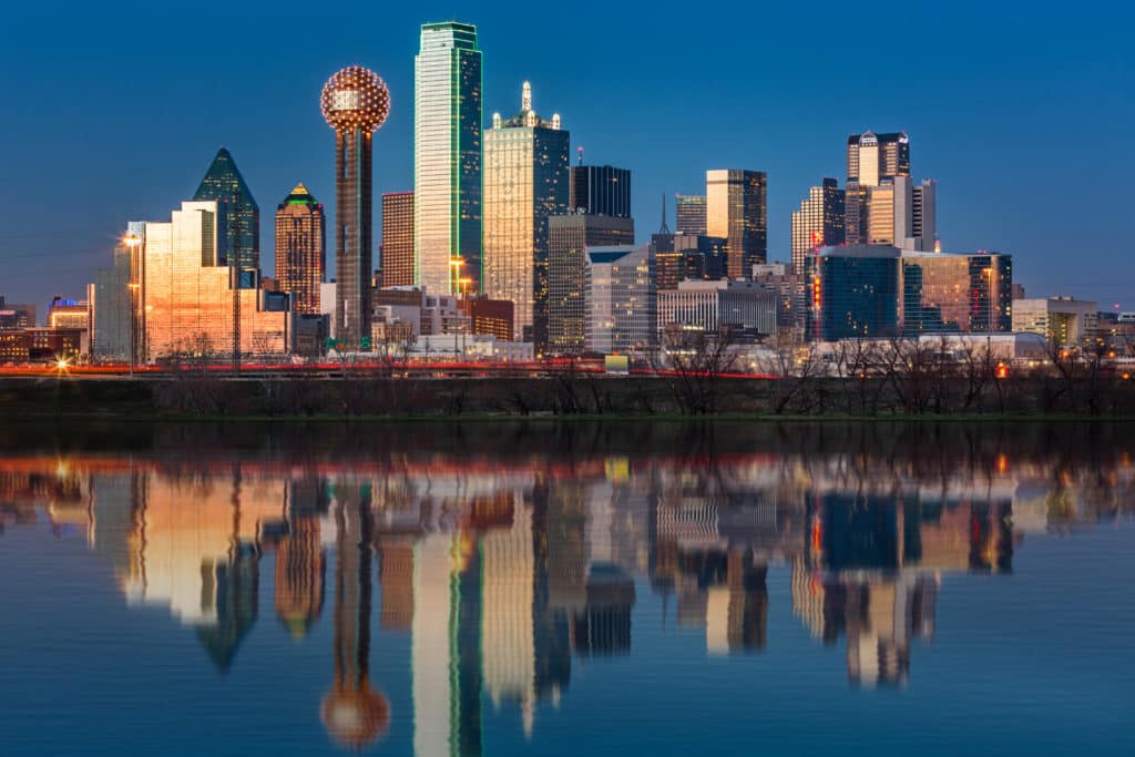 Downtown Dallas skyline at dusk with city lights reflecting on the water, highlighting the area served by US Legal Support Dallas court reporters