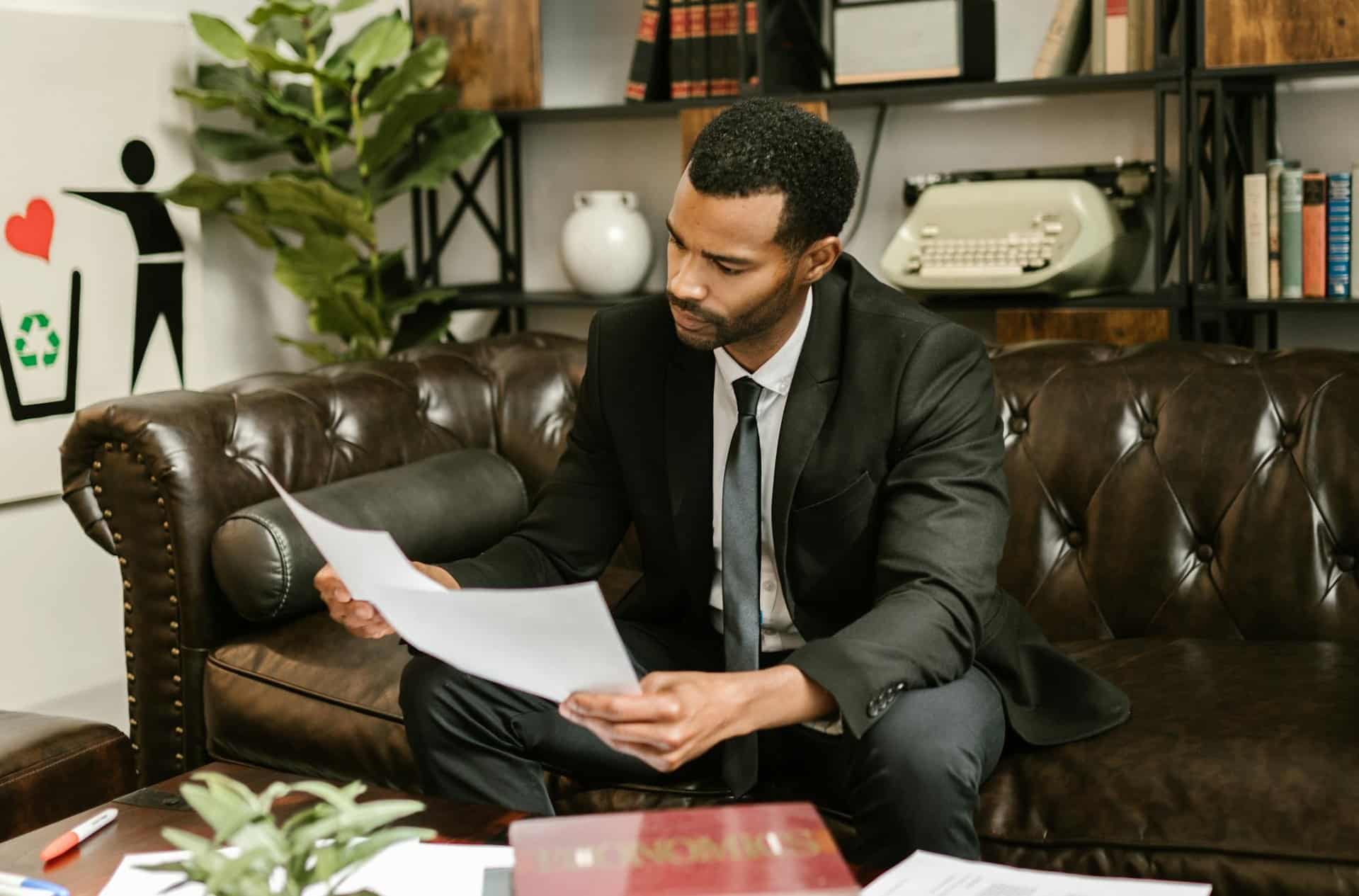 A lawyer sits on a leather couch, intensely reviewing legal documents.
