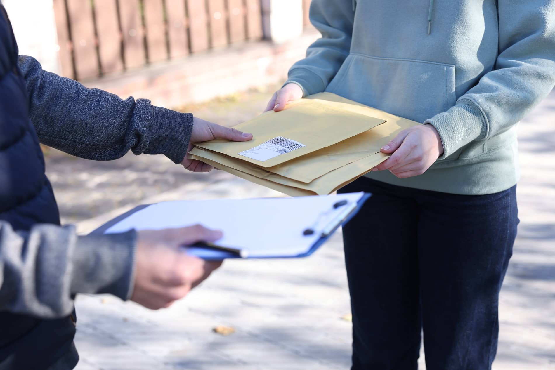 A process server handing padded legal envelopes to a recipient while holding a clipboard outdoors